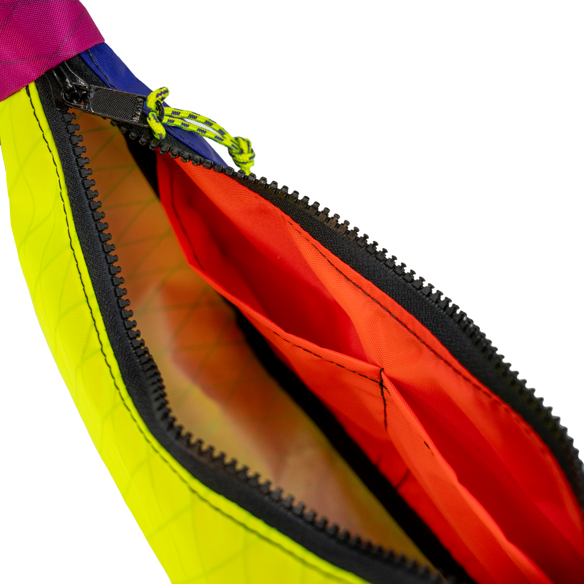 Close-up of a bright neon yellow-green bag with a black zipper, revealing a vivid orange interior lining and a small lime-green zipper pull on a white background.