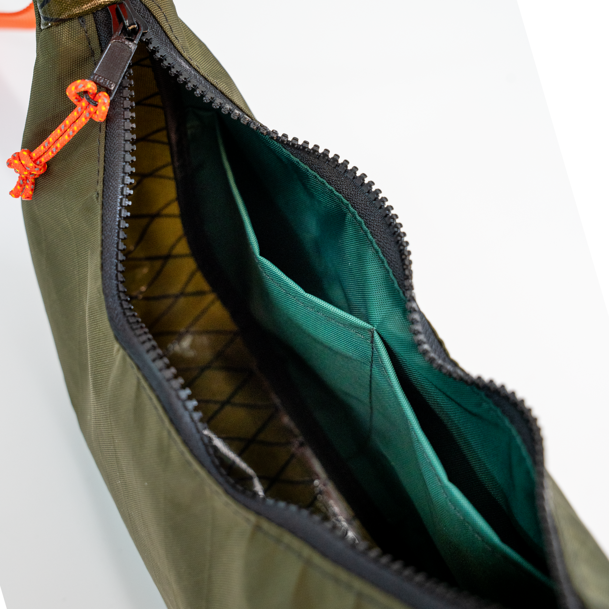 Close-up of an olive green nylon bag with a black zipper, bright orange drawcord zipper pull, and a dark green interior lining.